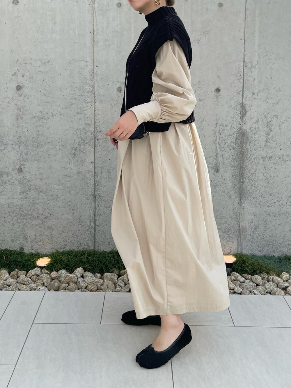 ブラック系のベスト、ベージュ系のワンピース、ブラック系のショルダーバッグを着用したレディースの秋コーディネートの2枚目の写真