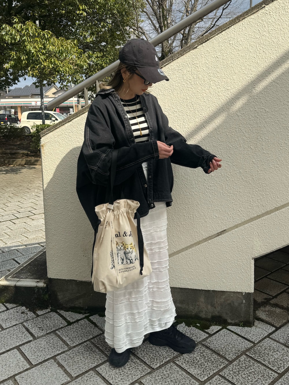 ベージュ系のトートバッグ、ブラック系のデニムジャケット、ホワイト系のスカートを着用したレディースの春コーディネートの3枚目の写真