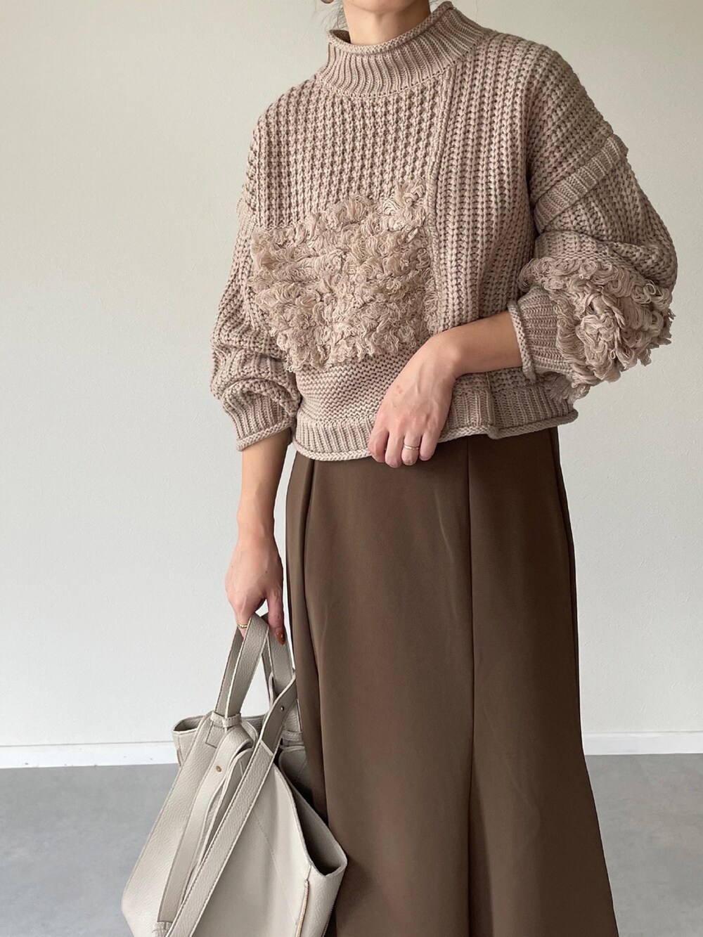 ベージュ系のニット/セーター、ブラウン系のスカート、ベージュ系のショルダーバッグを着用したレディースの秋コーディネートの4枚目の写真