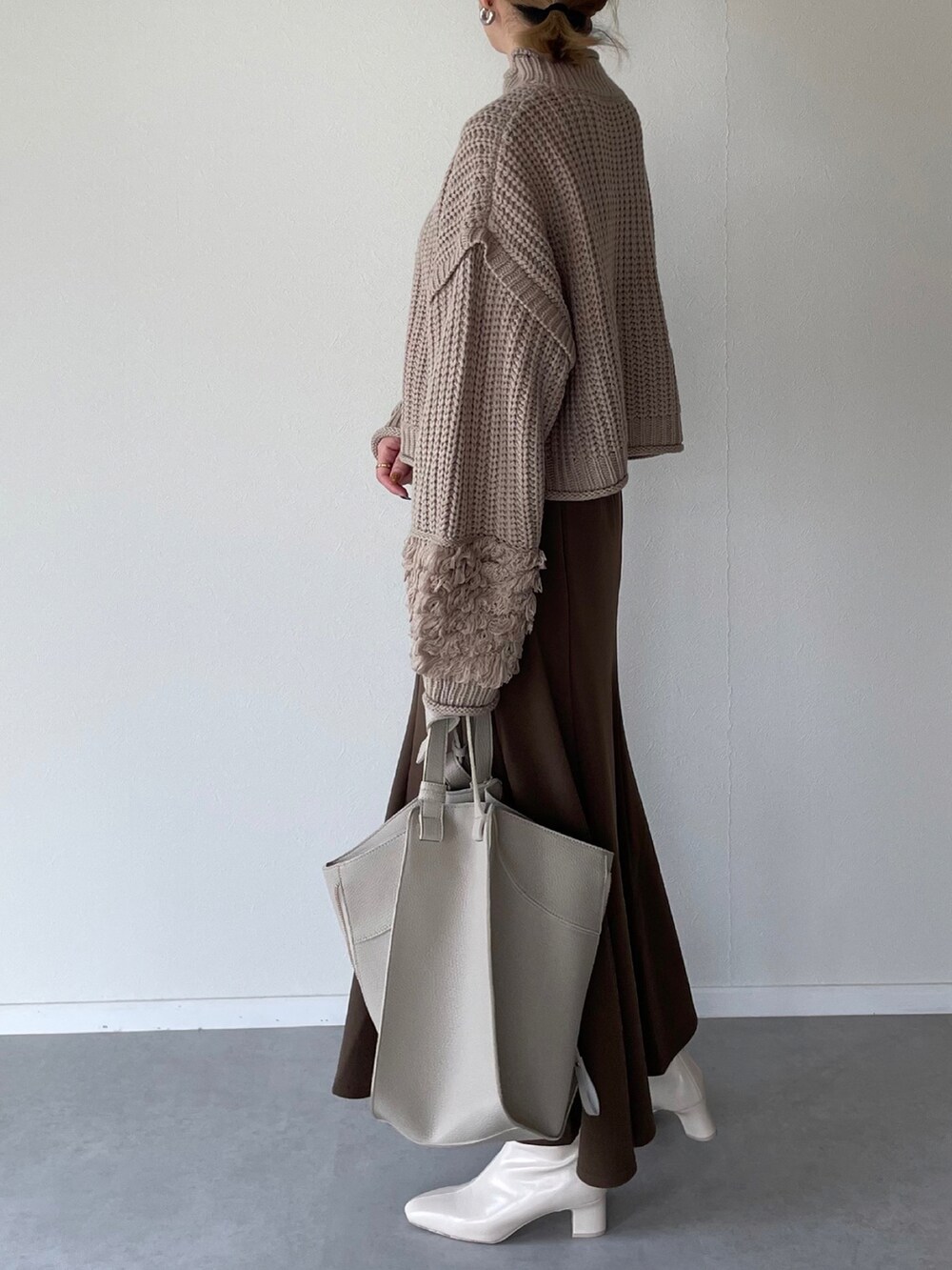ベージュ系のニット/セーター、ブラウン系のスカート、ベージュ系のショルダーバッグを着用したレディースの秋コーディネートの3枚目の写真