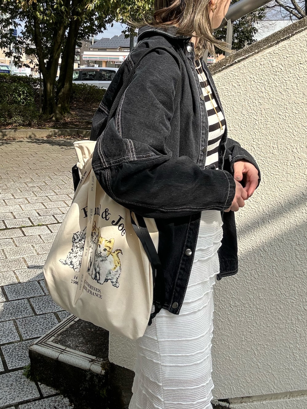 ベージュ系のトートバッグ、ブラック系のデニムジャケット、ホワイト系のスカートを着用したレディースの春コーディネートの5枚目の写真