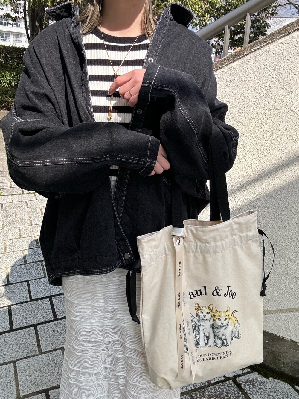 ベージュ系のトートバッグ、ブラック系のデニムジャケット、ホワイト系のスカートを着用したレディースの春コーディネートの4枚目の写真