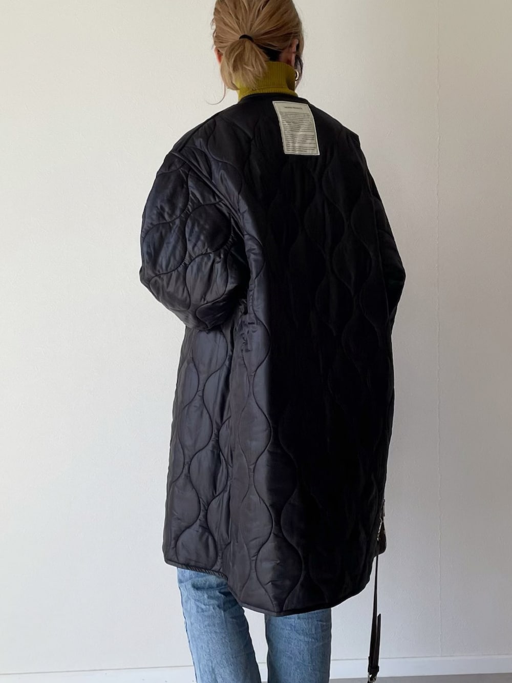 ブラック系のノーカラーコート、ブラウン系のショルダーバッグ、ブルー系のデニムパンツを着用したレディースの秋コーディネートの2枚目の写真