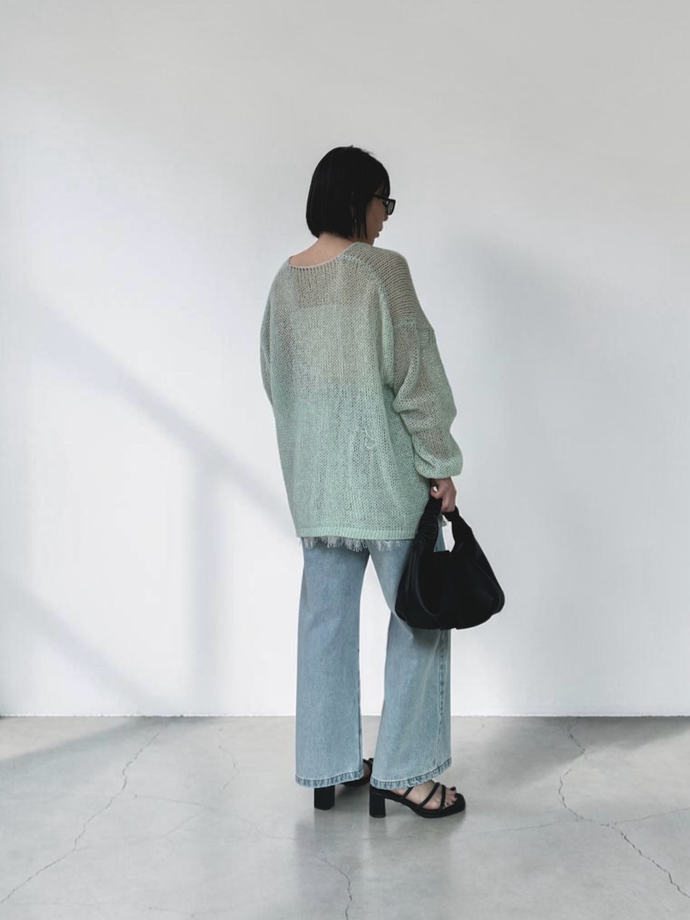 グリーン系のニット/セーター、ブラック系のショルダーバッグ、ブルー系のデニムパンツを着用したレディースの春コーディネートの3枚目の写真