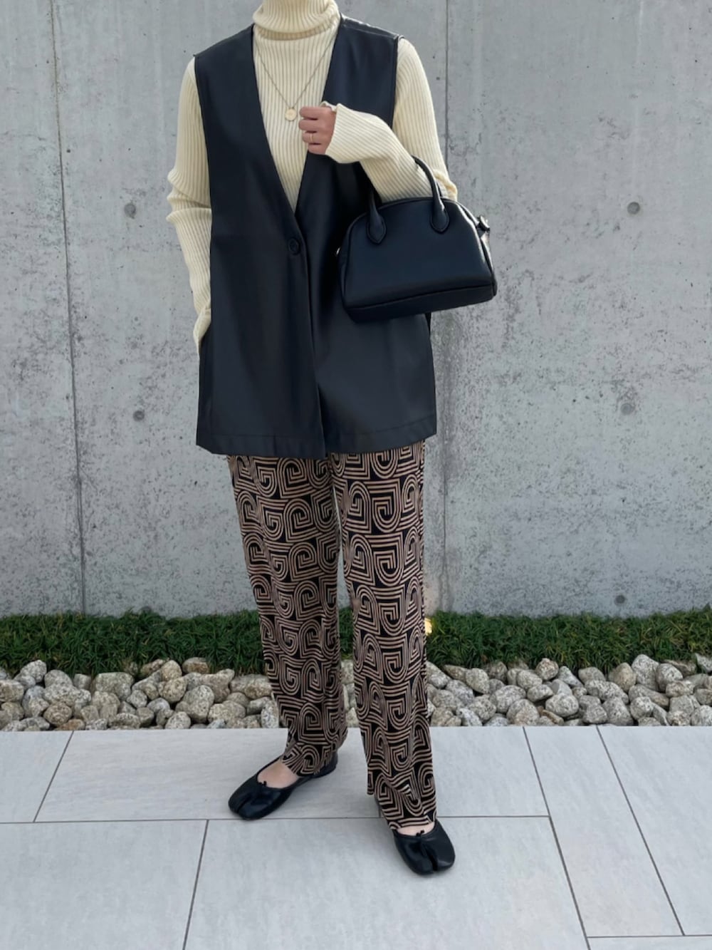 ブラック系のベスト、ホワイト系のニット/セーター、ブラック系のボストンバッグを着用したレディースの秋コーディネートの2枚目の写真