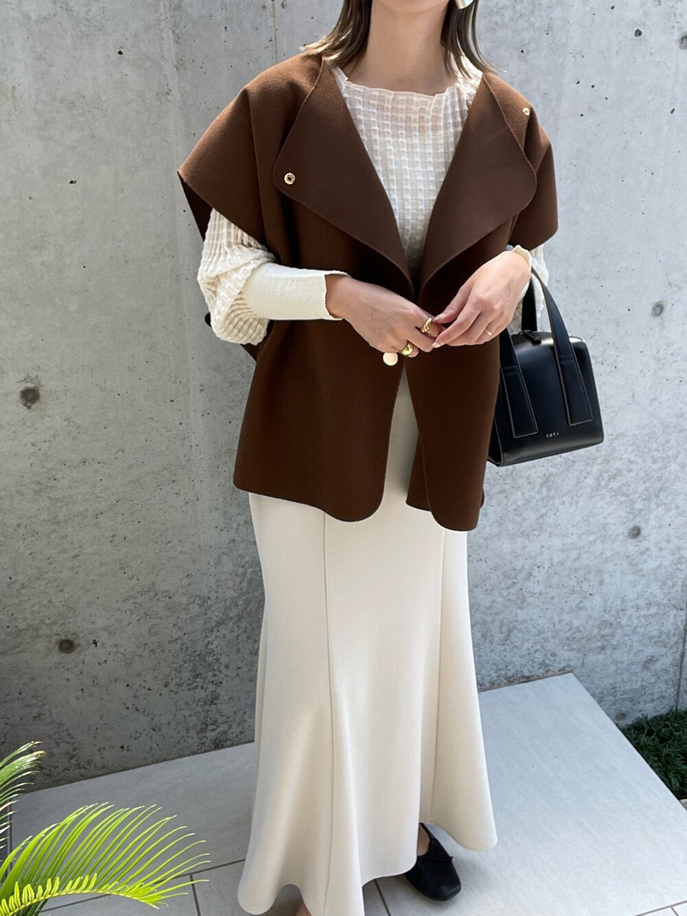 ブラウン系のベスト、ブラック系のボストンバッグ、ホワイト系のスカートを着用したレディースの夏コーディネートの3枚目の写真