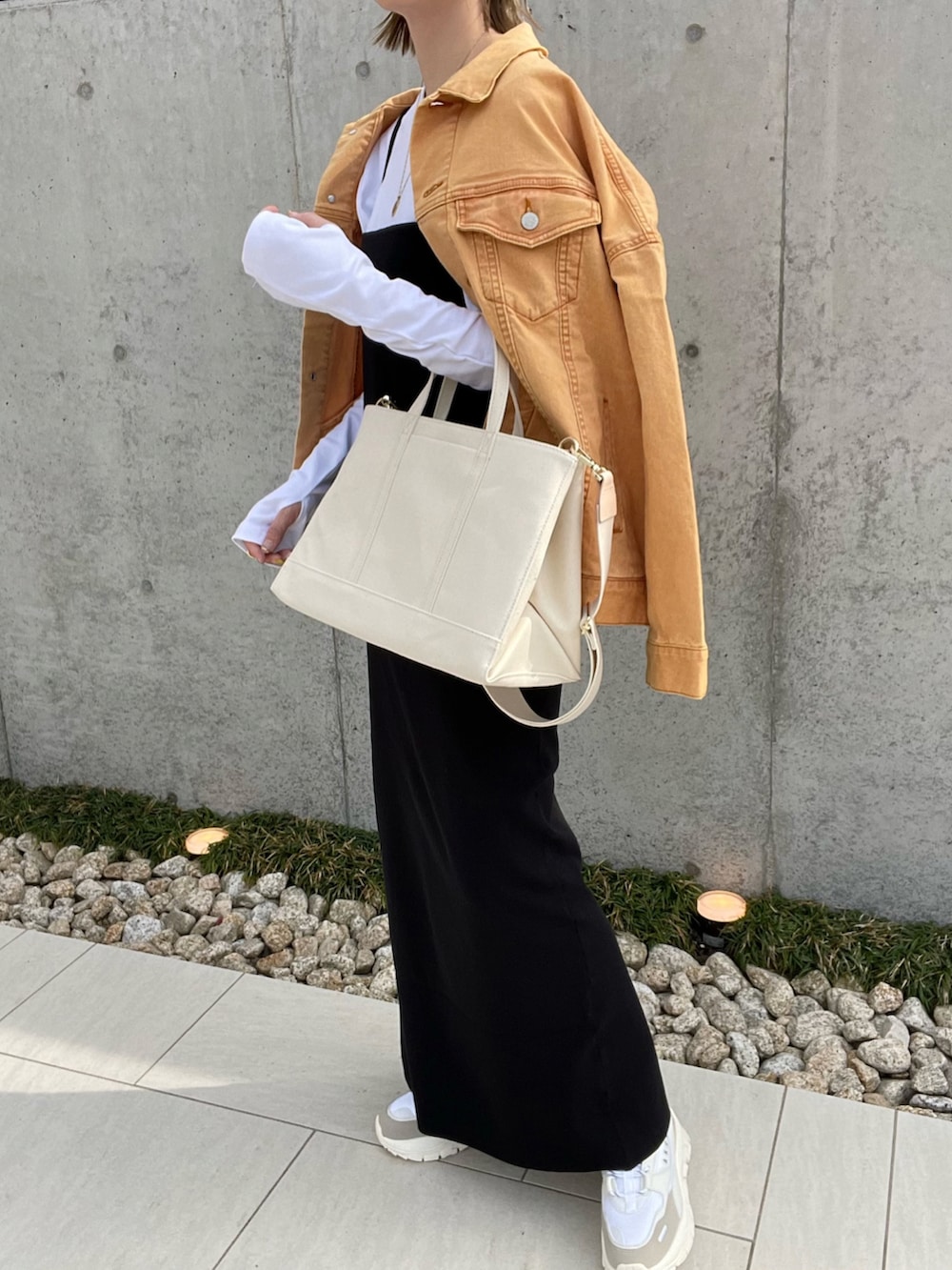 ホワイト系のトートバッグ、オレンジ系のデニムジャケット、ブラック系のワンピースを着用したレディースの春コーディネートの2枚目の写真
