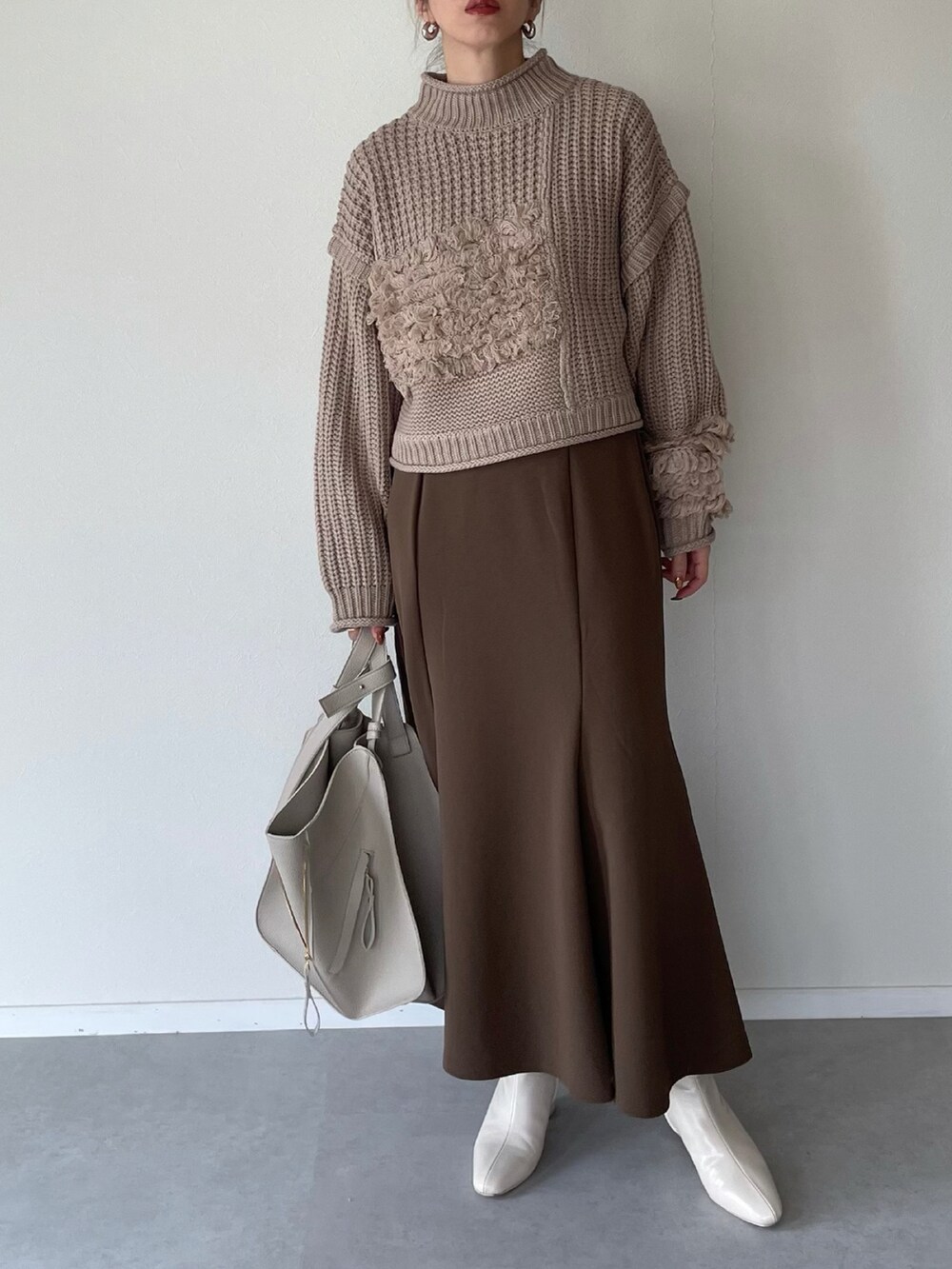 ベージュ系のニット/セーター、ブラウン系のスカート、ベージュ系のショルダーバッグを着用したレディースの秋コーディネートの2枚目の写真