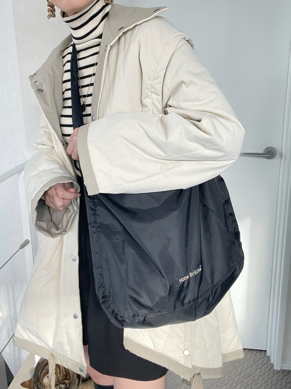 ブラック系のショルダーバッグ、ブラック系のニット/セーター、ホワイト系のダウンジャケット/コートを着用したレディースの冬コーディネートの4枚目の写真