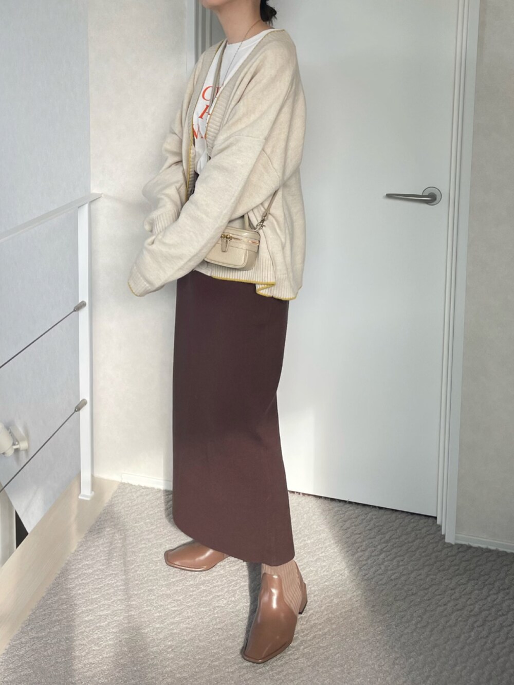 ホワイト系のカーディガン/ボレロ、ブラウン系のスカート、ブラウン系のブーツを着用したレディースの冬コーディネートの3枚目の写真