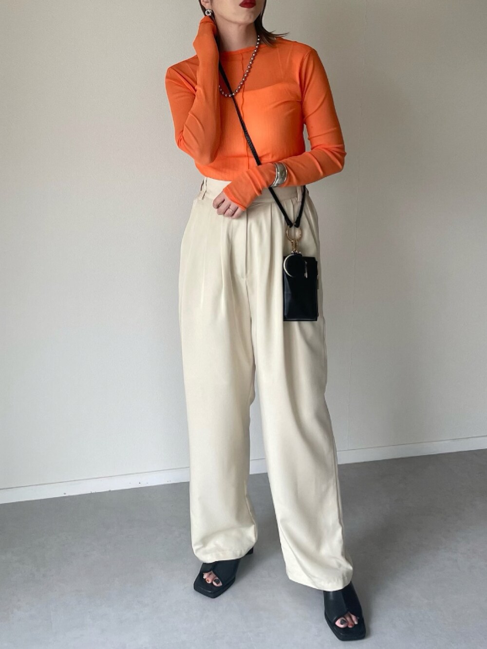 ホワイト系のスラックス、オレンジ系のTシャツ/カットソー、ブラック系のショルダーバッグを着用したレディースの夏コーディネートの2枚目の写真