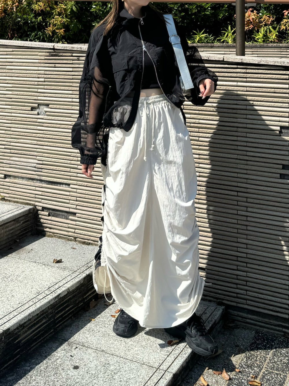 ホワイト系のスカート、ブラック系のブルゾン、シルバー系のショルダーバッグを着用したレディースの秋コーディネートの2枚目の写真