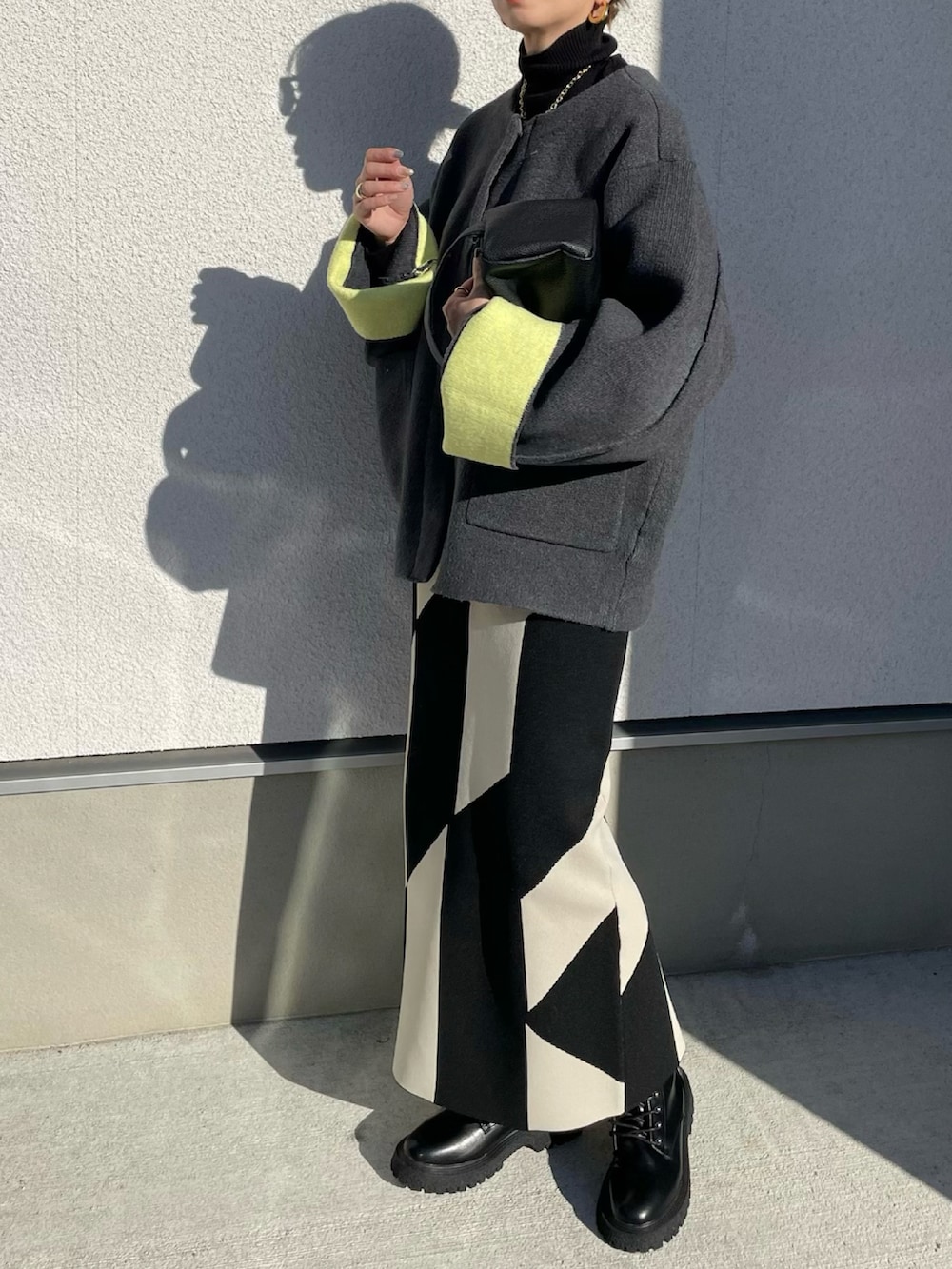 グレー系のノーカラーコート、ブラック系のブーツ、ブラック系のニット/セーターを着用したレディースの秋コーディネートの2枚目の写真