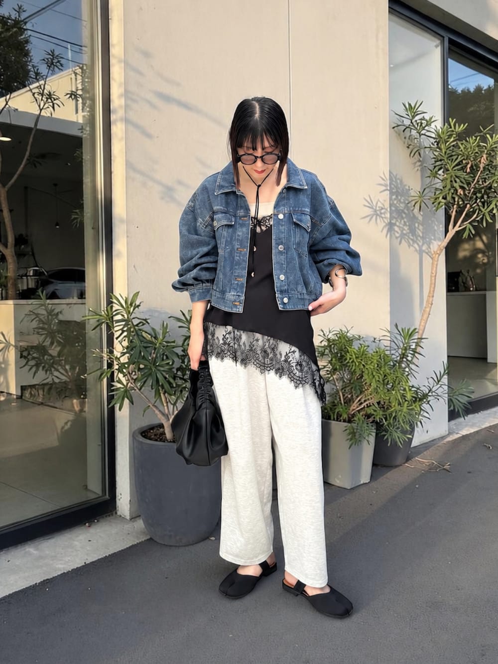 グレー系のデニムパンツ、ブラック系のショルダーバッグ、ブラック系のサンダルを着用したレディースの春コーディネートの2枚目の写真