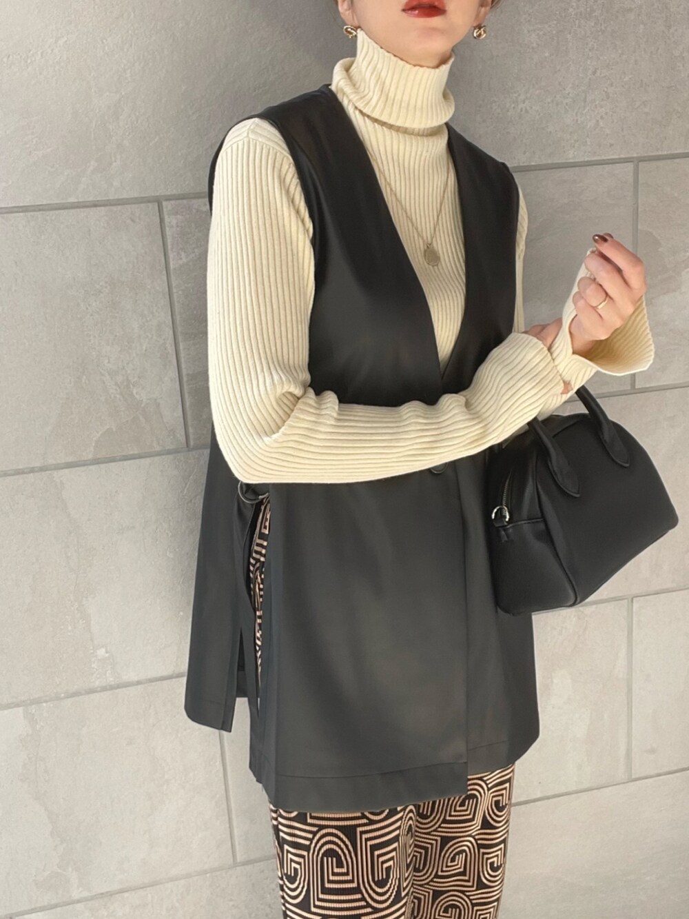 ブラック系のベスト、ホワイト系のニット/セーター、ブラック系のボストンバッグを着用したレディースの秋コーディネートの4枚目の写真