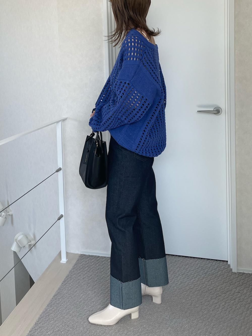 ブルー系のデニムパンツ、ブルー系のニット/セーター、ブラック系のハンドバッグを着用したレディースの春コーディネートの2枚目の写真