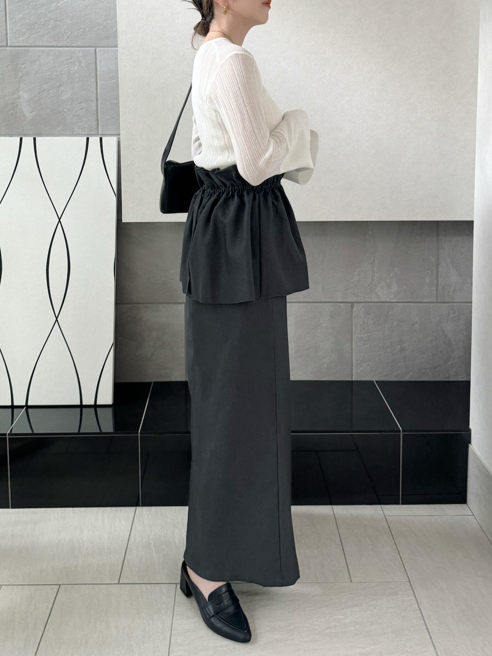 グレー系のスカート、ホワイト系のニット/セーター、ブラック系のローファーを着用したレディースの秋コーディネートの2枚目の写真