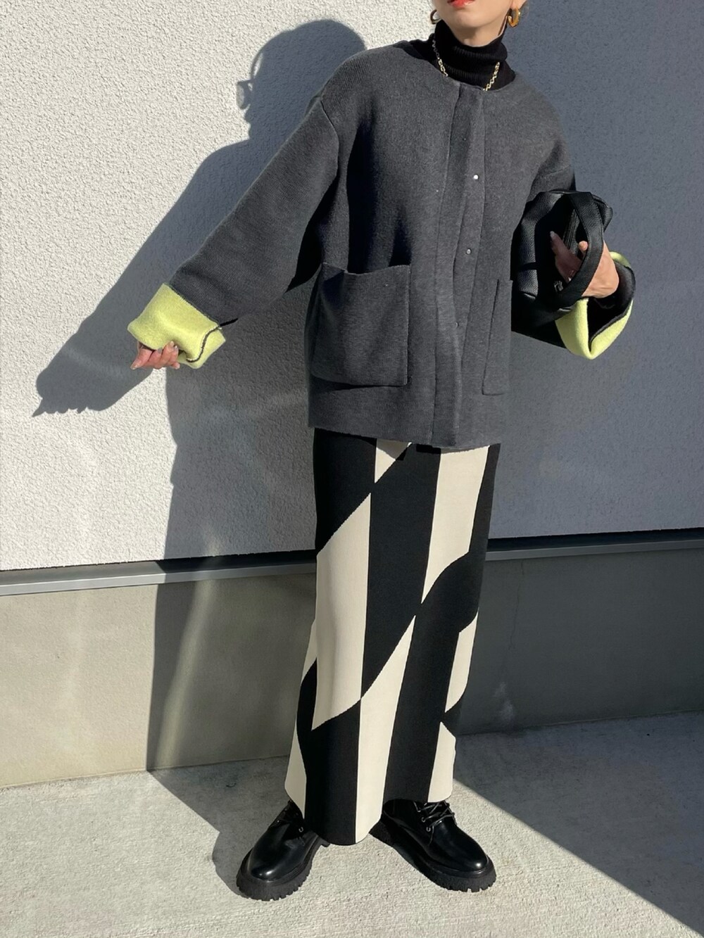 グレー系のノーカラーコート、ブラック系のブーツ、ブラック系のニット/セーターを着用したレディースの秋コーディネートの3枚目の写真