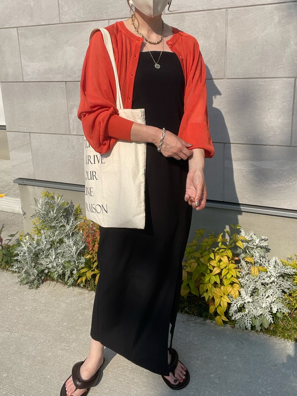 オレンジ系のカーディガン/ボレロ、ブラック系のワンピース、ブラウン系のサンダルを着用したレディースの春コーディネートの2枚目の写真