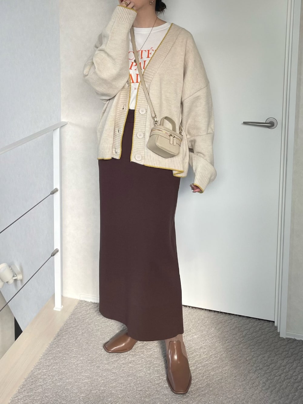 ホワイト系のカーディガン/ボレロ、ブラウン系のスカート、ブラウン系のブーツを着用したレディースの冬コーディネートの2枚目の写真