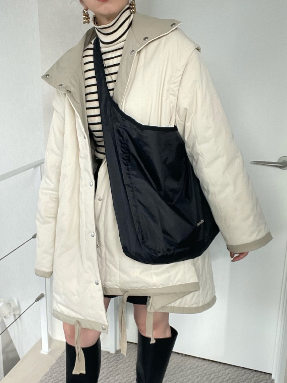 ブラック系のショルダーバッグ、ブラック系のニット/セーター、ホワイト系のダウンジャケット/コートを着用したレディースの冬コーディネートの3枚目の写真