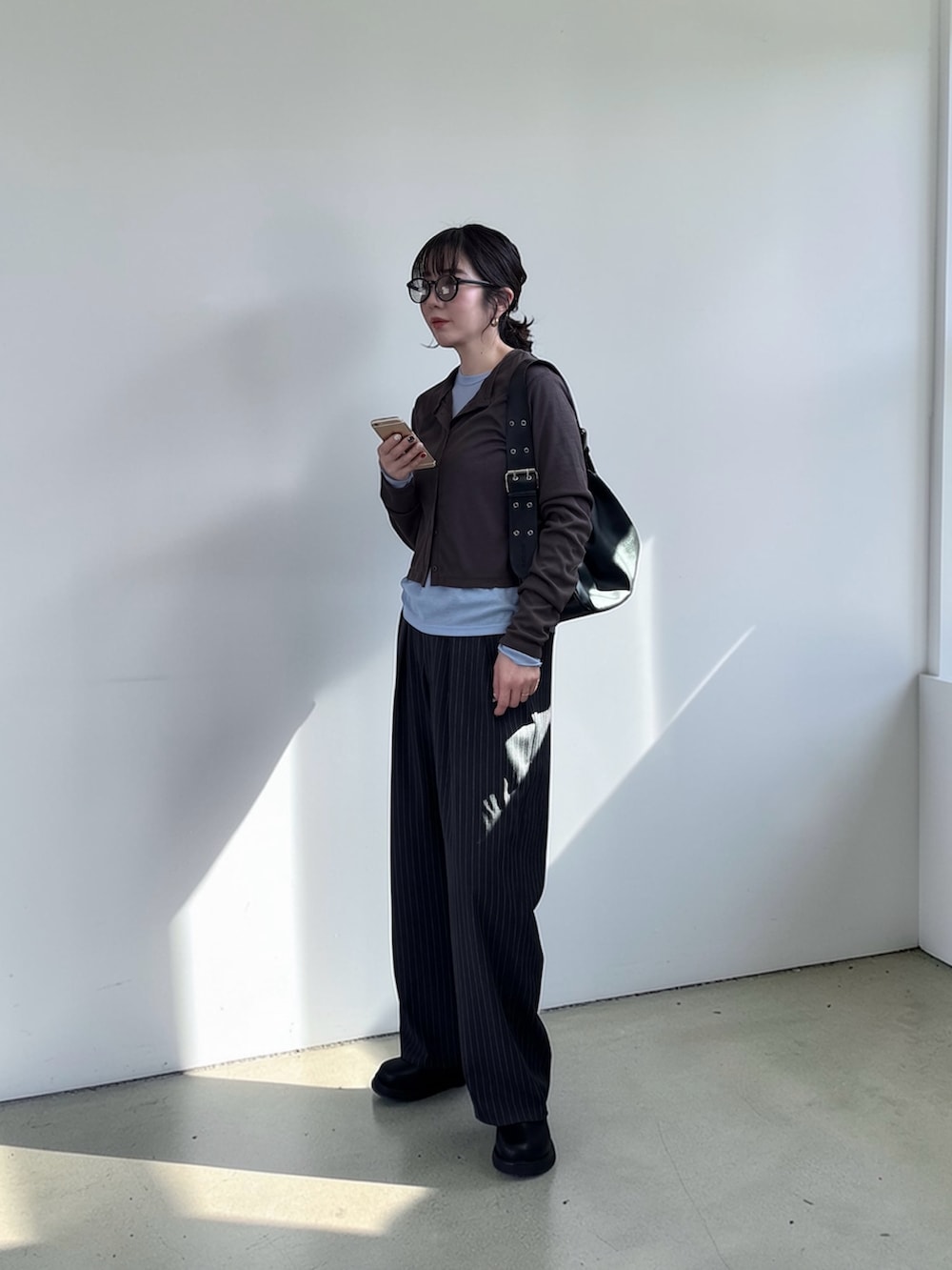 ブラウン系のカーディガン/ボレロ、グレー系のスラックス、ブラック系のハンドバッグを着用したレディースの春コーディネートの2枚目の写真