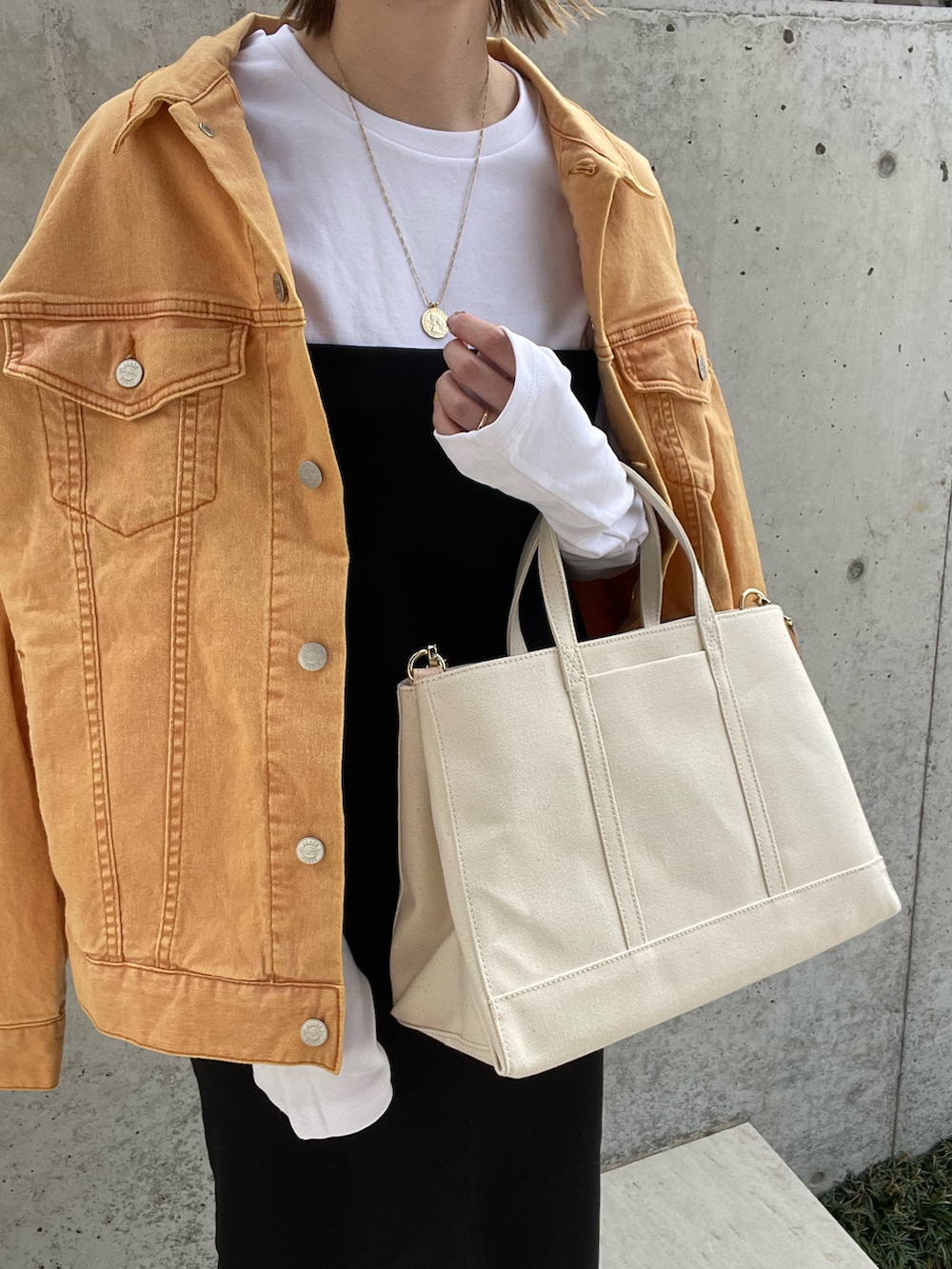 ホワイト系のトートバッグ、オレンジ系のデニムジャケット、ブラック系のワンピースを着用したレディースの春コーディネートの4枚目の写真