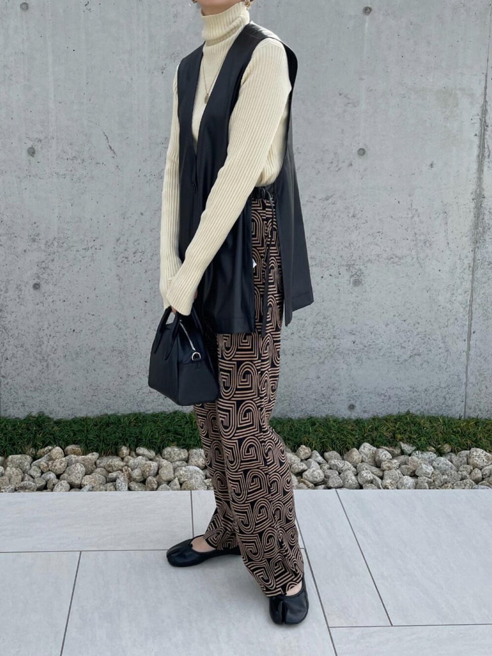 ブラック系のベスト、ホワイト系のニット/セーター、ブラック系のボストンバッグを着用したレディースの秋コーディネートの3枚目の写真