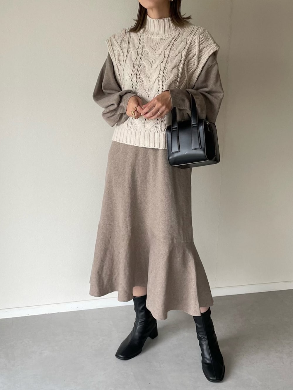 ホワイト系のベスト、ベージュ系のワンピース、ブラック系のボストンバッグを着用したレディースの秋コーディネートの4枚目の写真