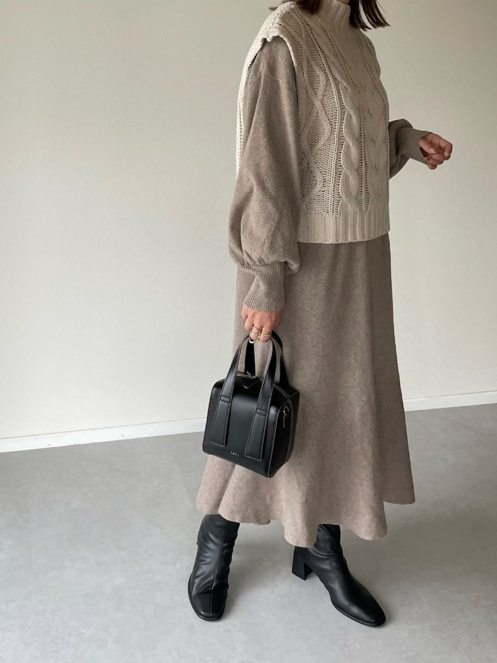 ホワイト系のベスト、ベージュ系のワンピース、ブラック系のボストンバッグを着用したレディースの秋コーディネートの2枚目の写真