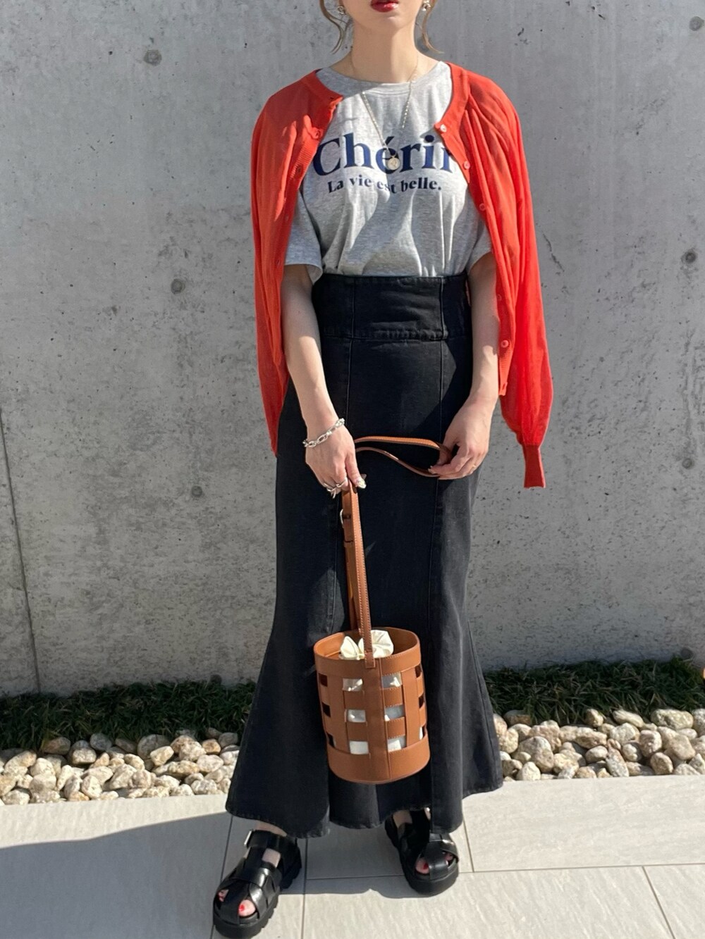 グレー系のTシャツ/カットソー、ブラック系のスカート、オレンジ系のカーディガン/ボレロを着用したレディースの春コーディネートの2枚目の写真