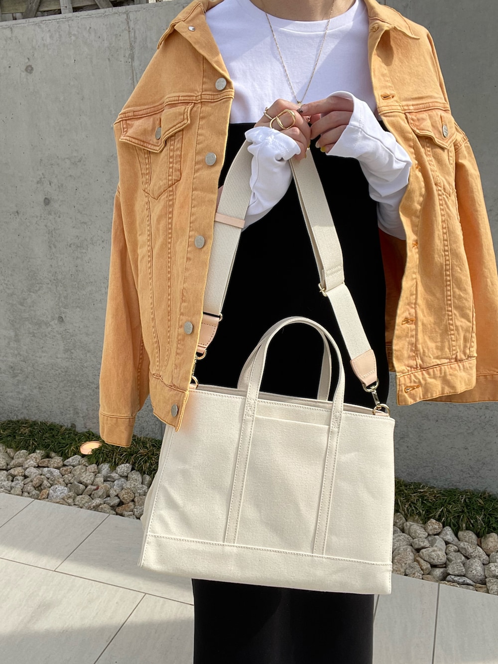 ホワイト系のトートバッグ、オレンジ系のデニムジャケット、ブラック系のワンピースを着用したレディースの春コーディネートの5枚目の写真