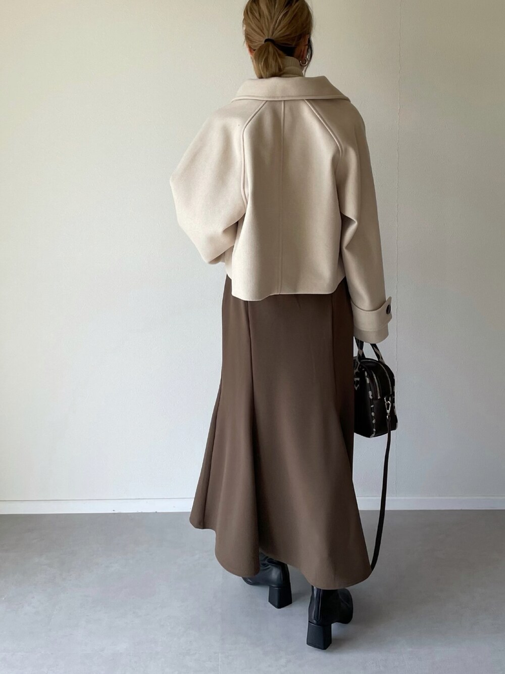 ホワイト系のその他アウター、ブラウン系のスカート、ブラック系のブーツを着用したレディースの秋コーディネートの2枚目の写真