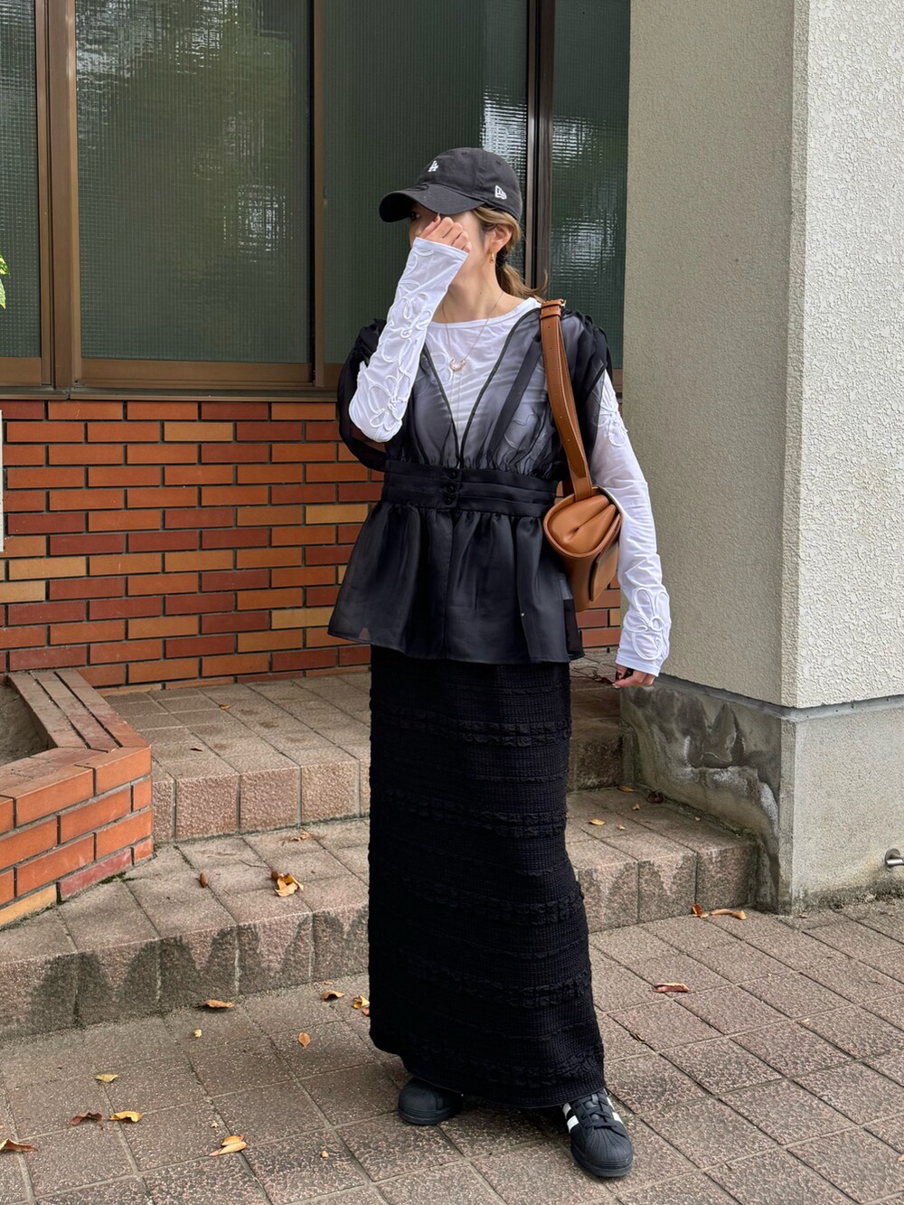 ホワイト系のTシャツ/カットソー、ブラック系のスカート、ブラック系のスニーカーを着用したレディースの秋コーディネートの2枚目の写真