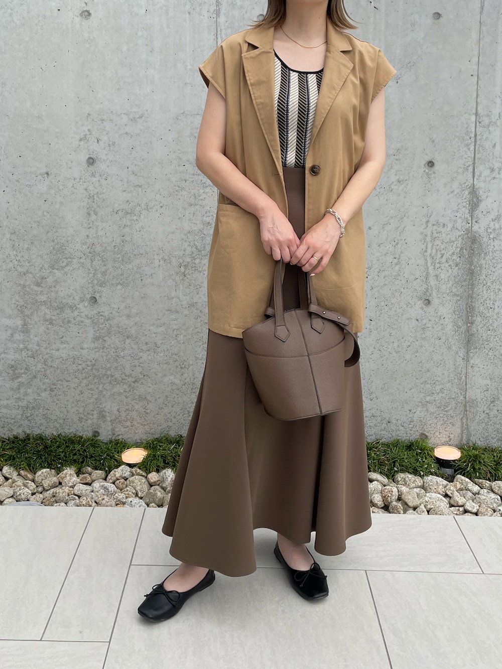 イエロー系のベスト、ブラウン系のスカート、ブラック系のパンプスを着用したレディースの夏コーディネートの2枚目の写真