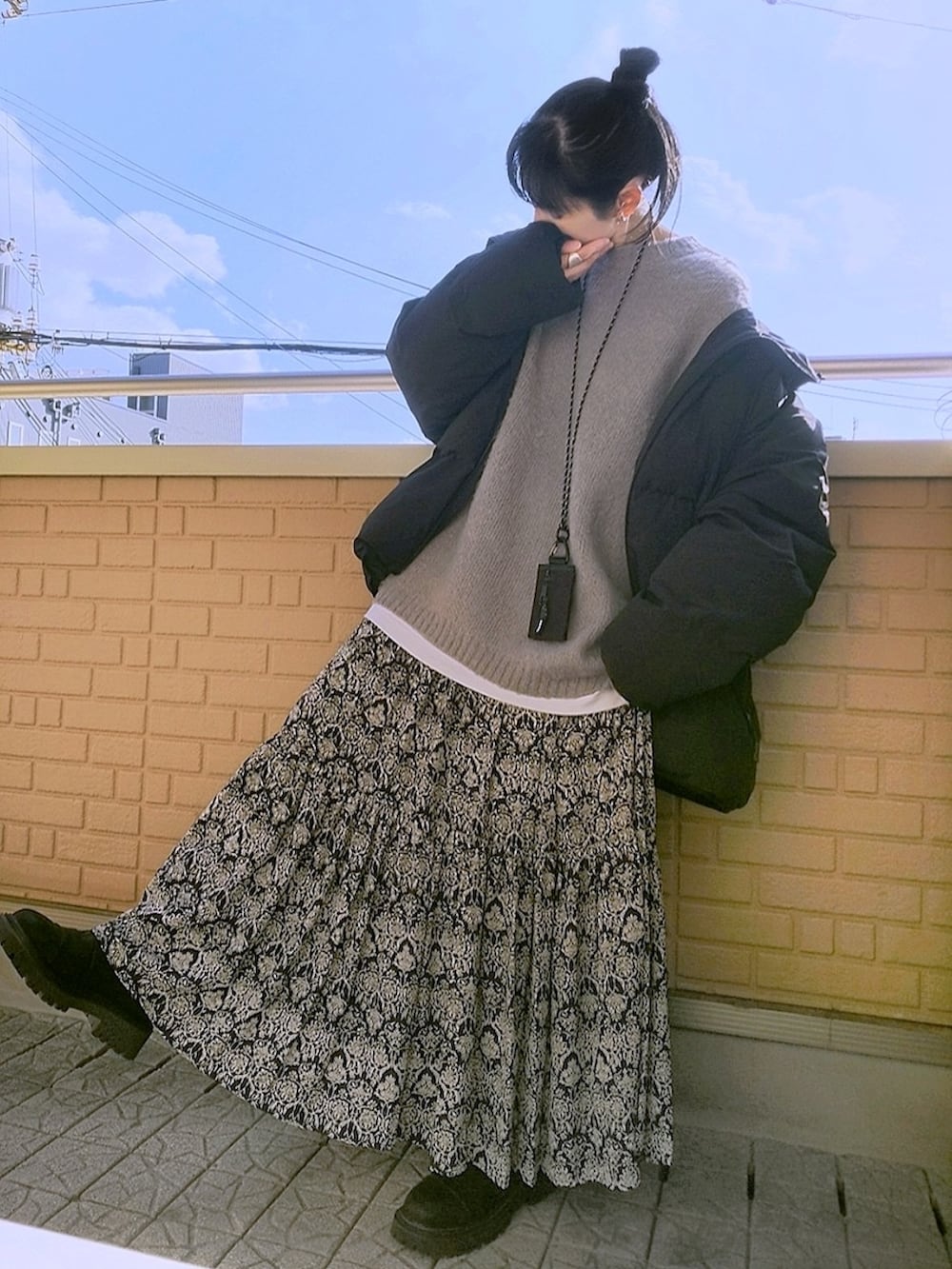 グレー系のニット/セーター、ブラック系のスカート、ブラック系のブーツを着用したレディースの冬コーディネートの2枚目の写真