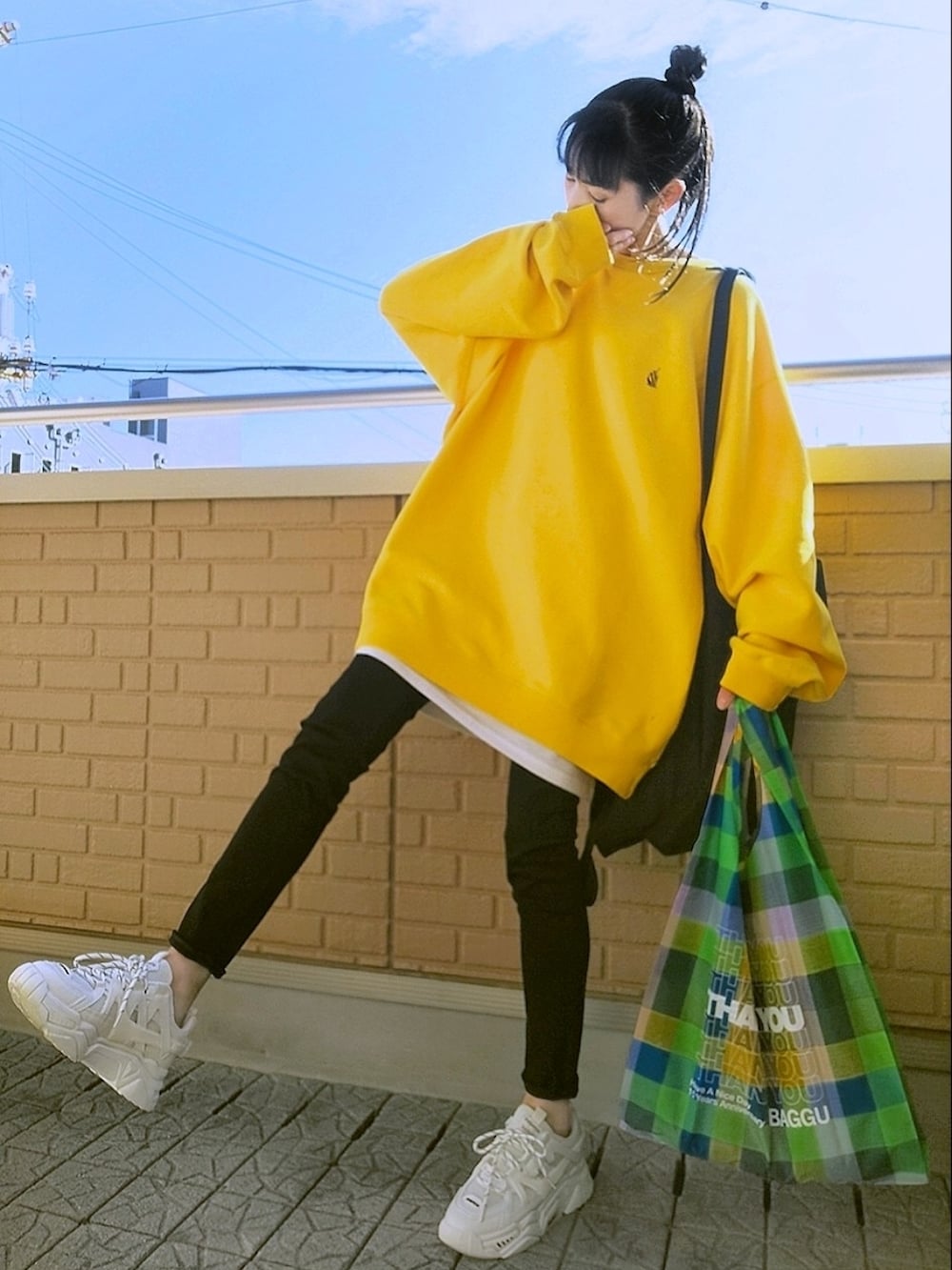 イエロー系のスウェット、ブラック系のデニムパンツ、ホワイト系のスニーカーを着用したレディースの秋コーディネートの2枚目の写真