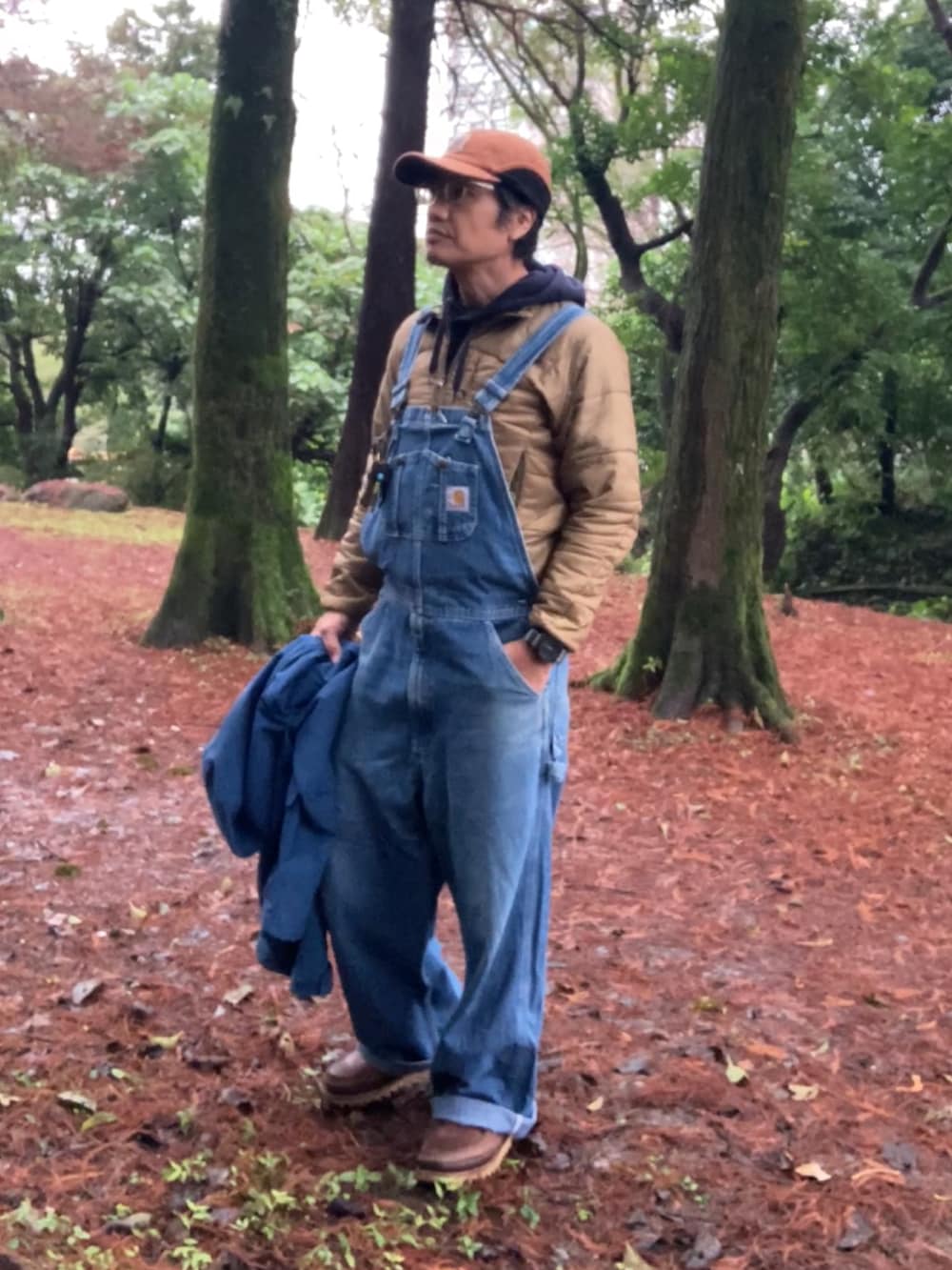 ブルー系のサロペット/オーバーオール、ブルー系のマウンテンパーカー、ブラウン系のブーツを着用したメンズの冬コーディネートの2枚目の写真