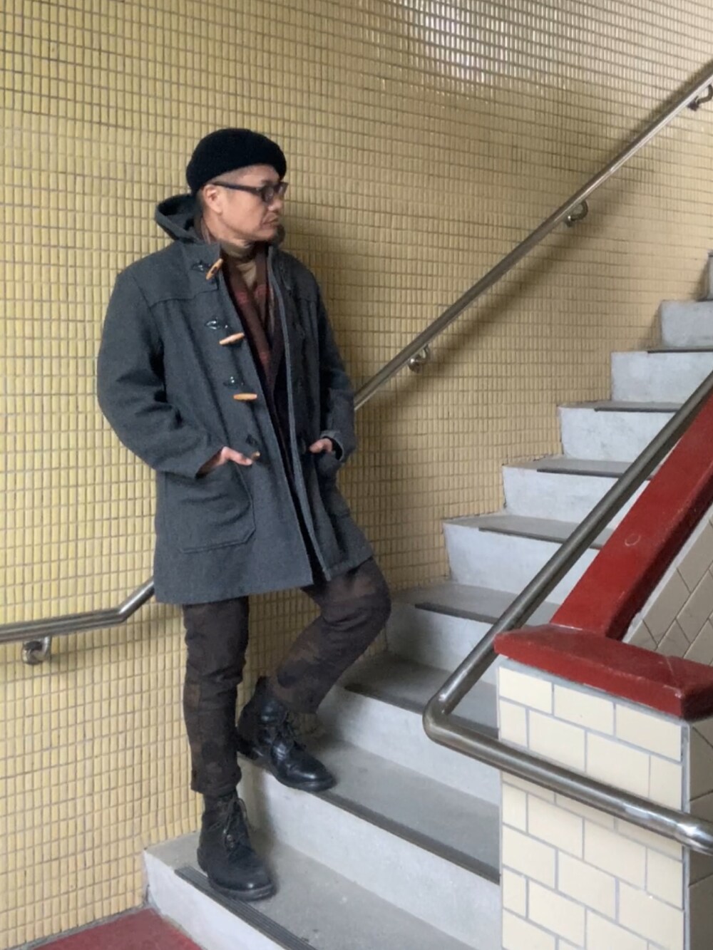 グレー系のダッフルコート、ブラウン系のニット/セーター、ブラック系のテーラードジャケットを着用したメンズの冬コーディネートの2枚目の写真