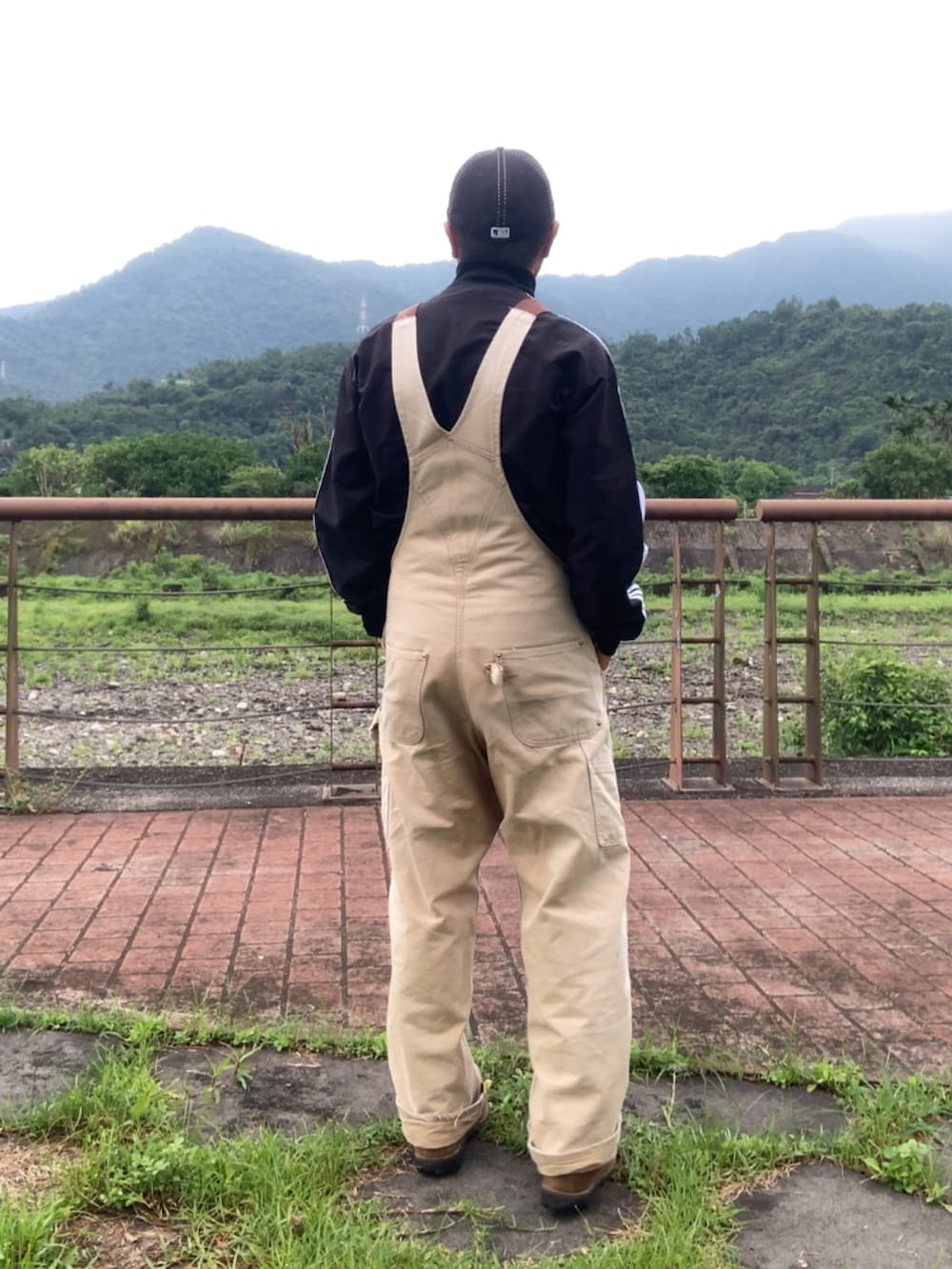 ブラウン系のサロペット/オーバーオール、ブラック系のジャージ、ブラウン系のブーツを着用したメンズの春コーディネートの2枚目の写真