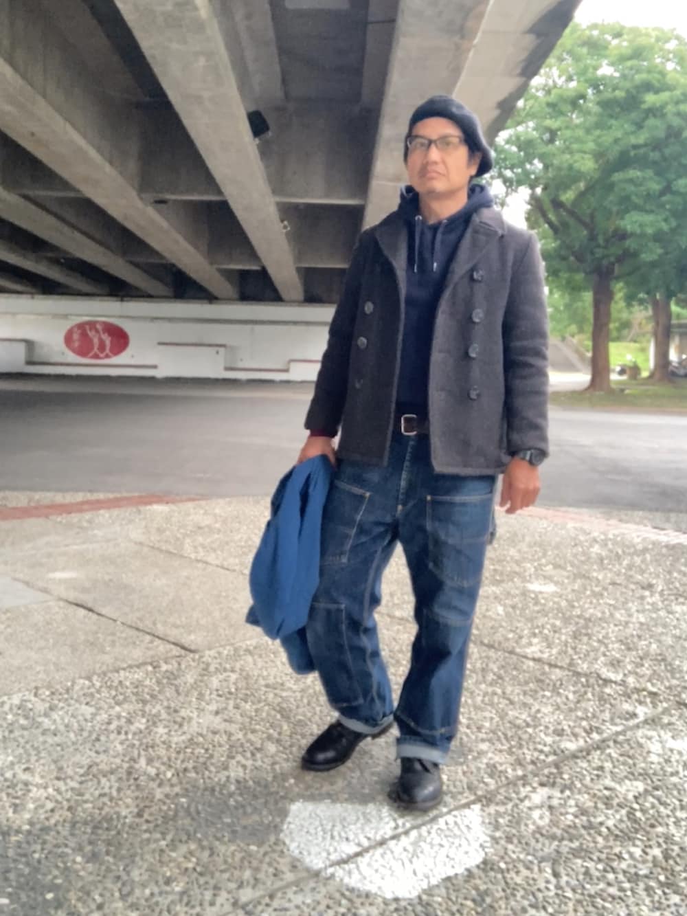 グレー系のピーコート、ブルー系のパーカー、ブルー系のデニムパンツを着用したメンズの冬コーディネートの2枚目の写真