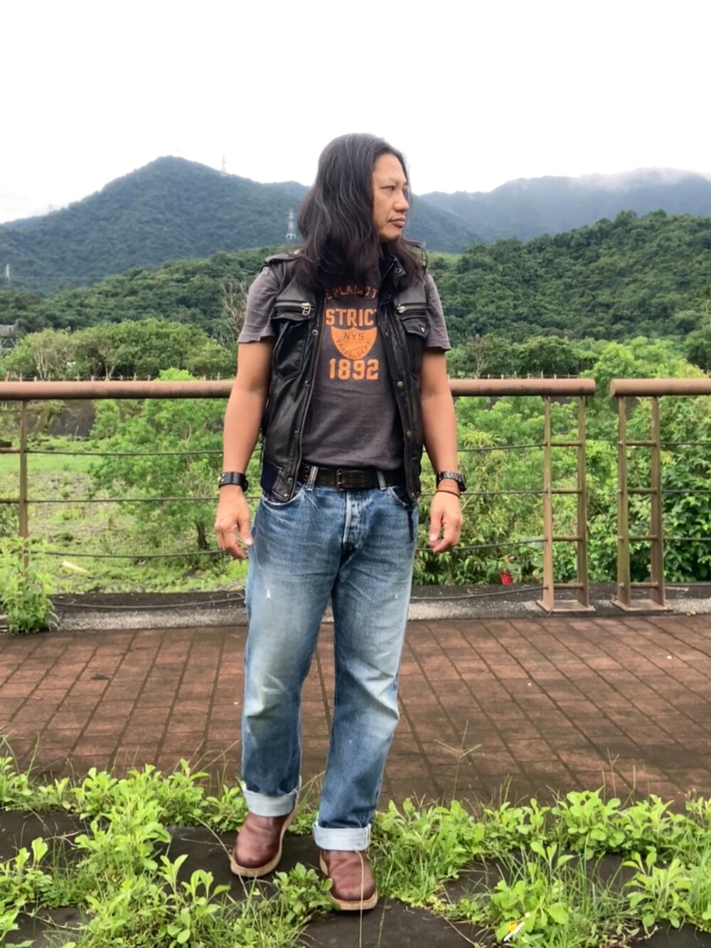 ブラウン系のスリッポン、ブルー系のデニムパンツ、ブラック系のミリタリージャケットを着用したメンズの夏コーディネートの2枚目の写真