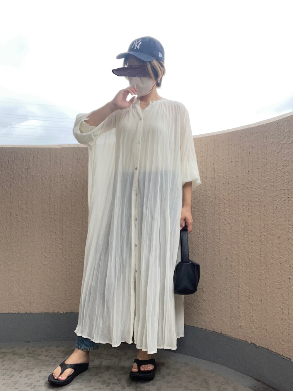 ホワイト系のワンピース、ブラック系のサンダル、ブラック系のハンドバッグを着用したレディースの夏コーディネートの2枚目の写真