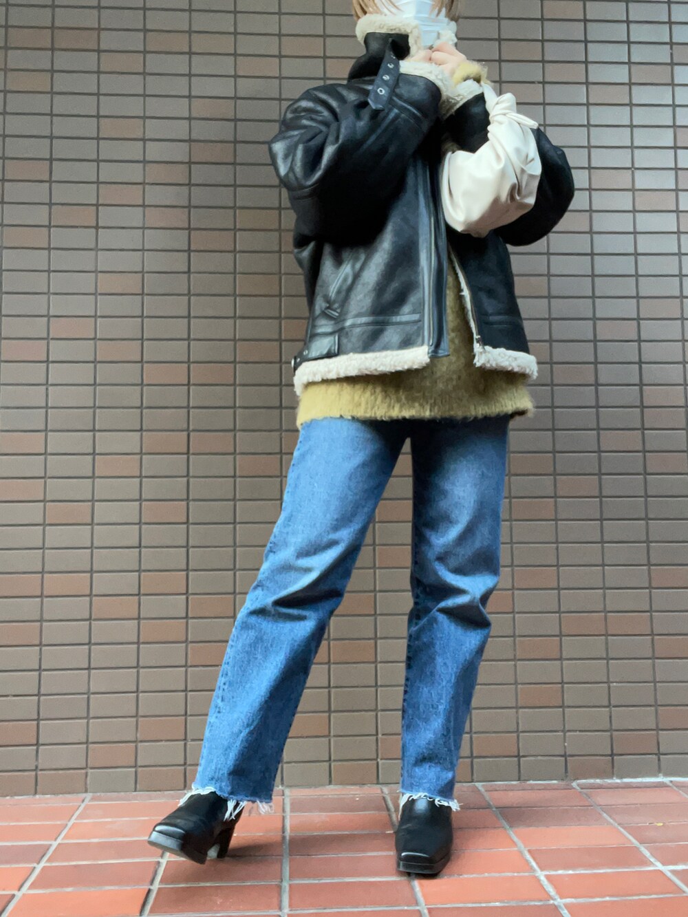 ブルー系のデニムパンツ、ブラック系のブーツ、ホワイト系のハンドバッグを着用したレディースの冬コーディネートの2枚目の写真