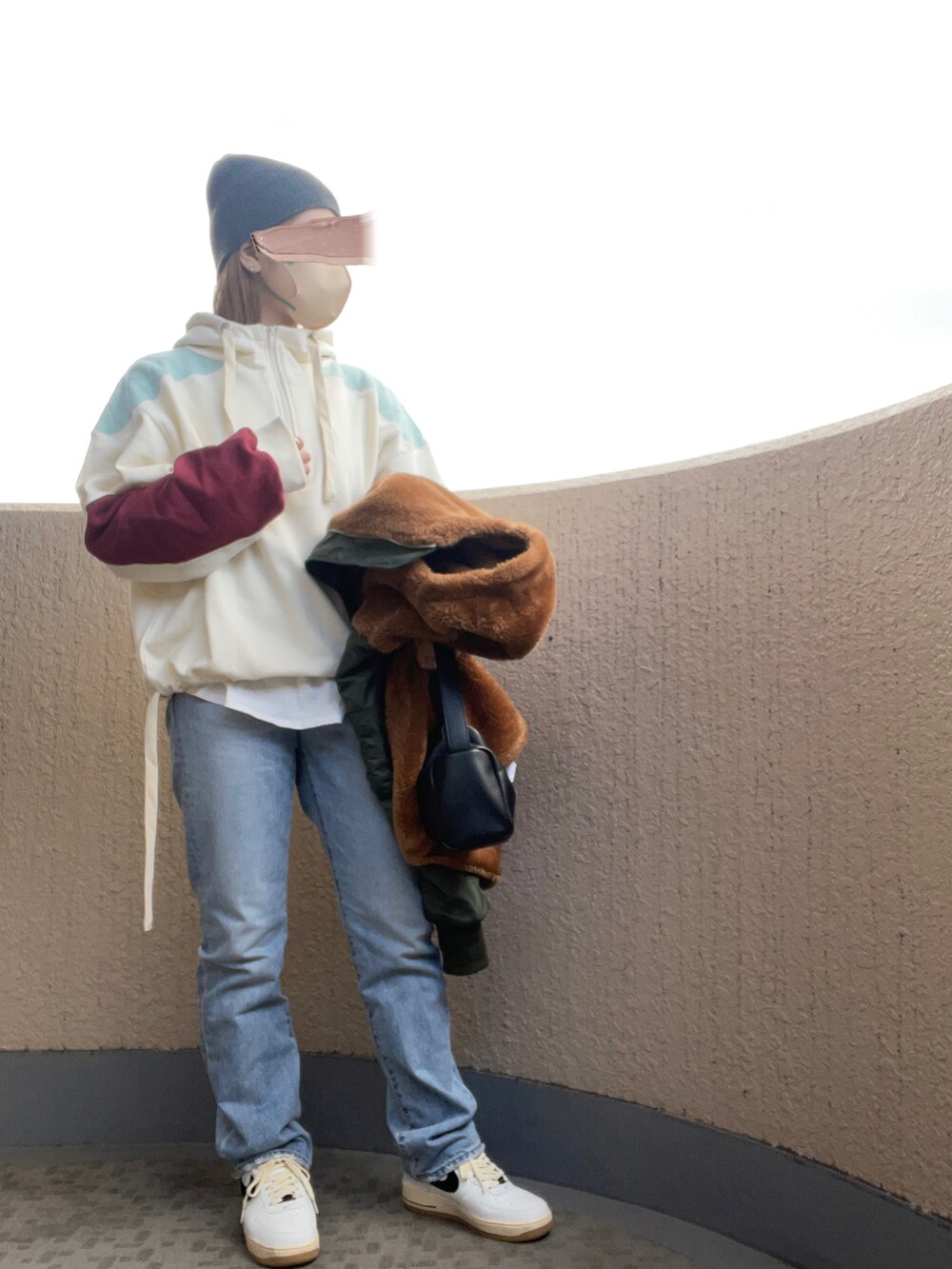 ブルー系のデニムパンツ、ホワイト系のスニーカー、ブラック系のハンドバッグを着用したレディースの冬コーディネートの2枚目の写真