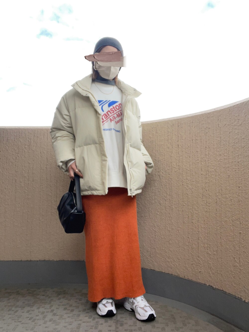 オレンジ系のスカート、ホワイト系のスニーカー、ブラック系のハンドバッグを着用したレディースの冬コーディネートの2枚目の写真