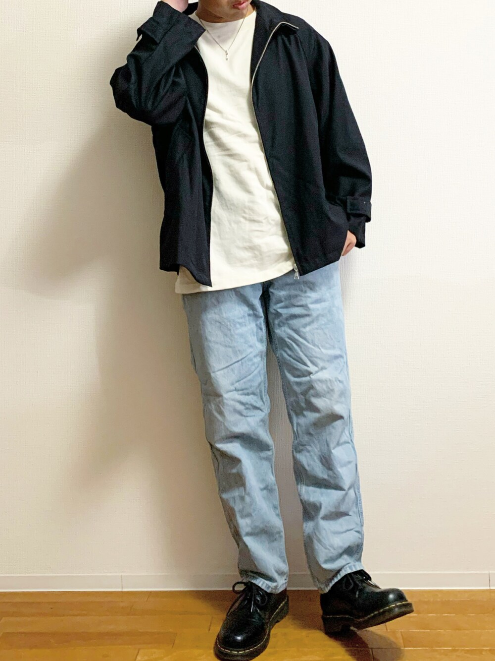 ブラック系のブルゾン、ベージュ系のTシャツ/カットソー、ブルー系のデニムパンツを着用したメンズの秋コーディネートの2枚目の写真