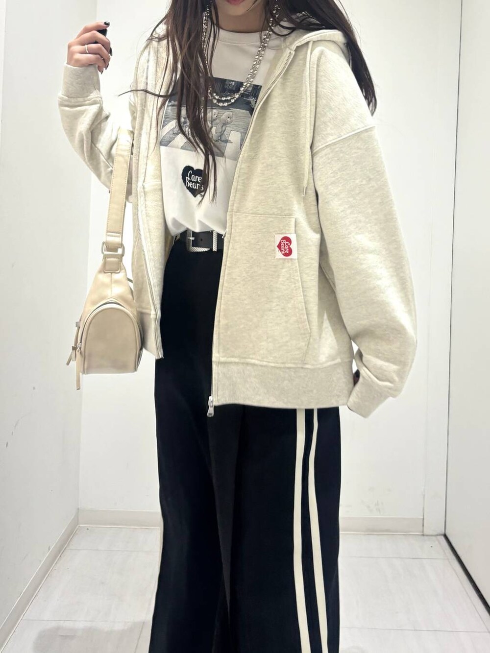 ホワイト系のショルダーバッグ、ブラック系のスラックス、ベージュ系のパーカーを着用したレディースの春コーディネートの4枚目の写真