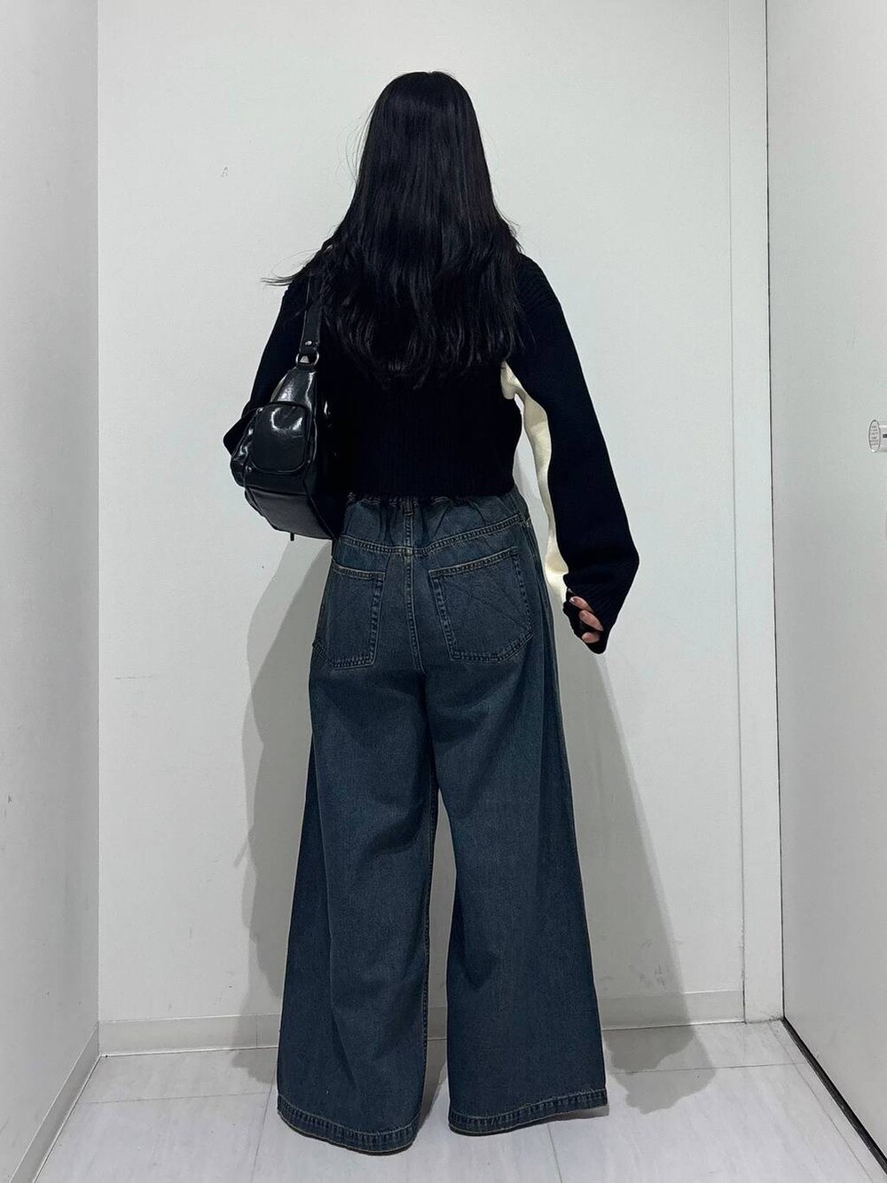 ブルー系のデニムパンツ、ブラック系のショルダーバッグ、ブラック系のニット/セーターを着用したレディースの秋コーディネートの4枚目の写真