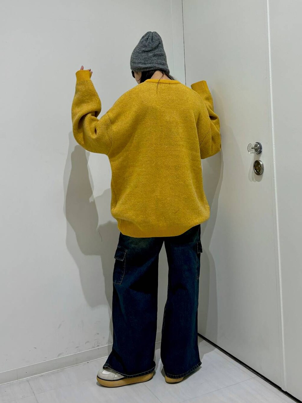 イエロー系のニット/セーター、ブルー系のデニムパンツ、グレー系のニットキャップ/ビーニーを着用したレディースの冬コーディネートの4枚目の写真